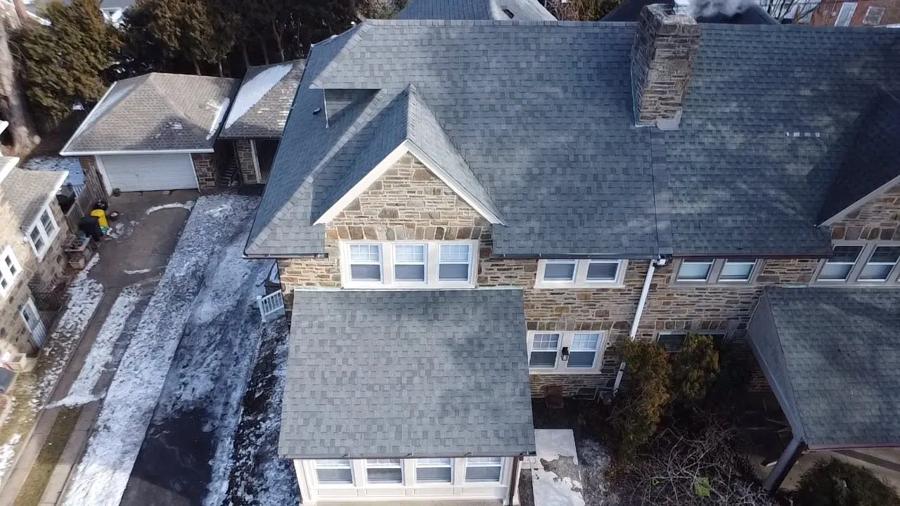 Drone view of a stone house with a new slate-style shingle roof in the snow
