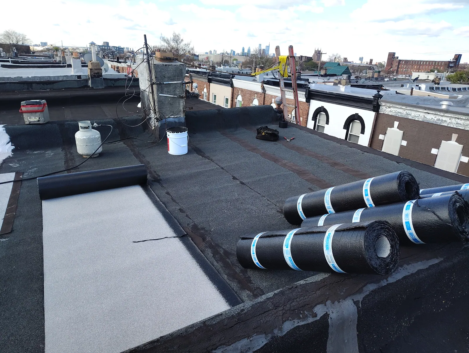 Rolls of roofing cap sheet staged on a Philadelphia rowhome roof during a Made in America Roofing job